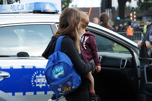 kobieta trzyma na rękach dziecko, za nimi oznakowany radiowóz
