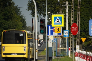 jadący drogą żółty autobus, obok znaki drogowe
