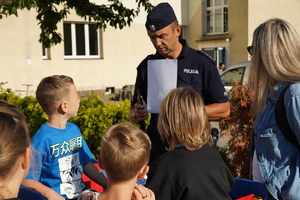 policjant trzyma kolorowankę i rozmawia z uczniami szkoły podstawowej