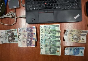 banknoty poukładane na blacie biurka, obok nich laptop