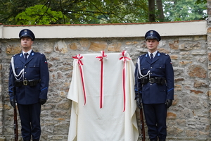 policjanci asysty honorowej stoją przy zasłoniętej płótnem tablicy. Na płótnie biało-czerwone wstążki