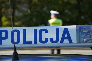 napis POLICJA na radiowozie, w tle policjant