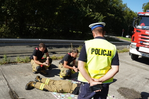 strażacy wykonują pokaz pierwszej pomocy, policjant przygląda się