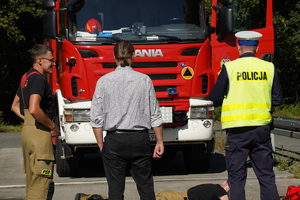 policjant, kierowca osobówki oraz strażak zwróceni twarzą w kierunku wozu strażackiego