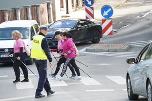 policjant drogówki w odblaskowej kamizelce, ludzie przechodzący przez oznakowane przejście