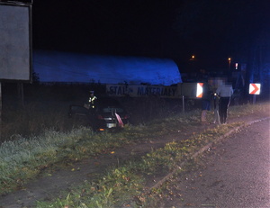 łuk drogi, samochód w rowie, przy drodze stoją ludzie. Obok samochodu policjant. Jest ciemno