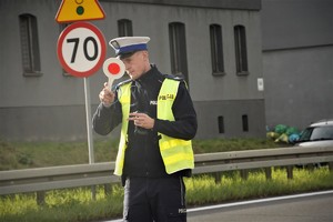 policjant drogówki trzyma w ręce tarczę, potocznie zwaną lizakiem, zatrzymuje do kontroli samochód