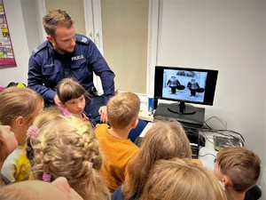 dzielnicowy otoczony grupą dzieci. Scena ma miejsce w komisariacie