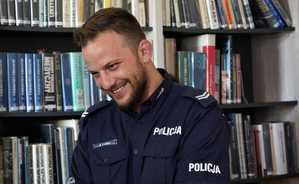 policjant uśmiecha się, za nim regał z książkami