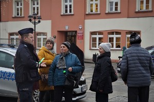 policjant otoczony grupą seniorów rozdaje odblaskowe opaski