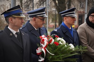 delegacja mundurowych, jeden z nich trzyma wiązankę kwiatów