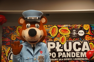policyjna maskotka na tle baneru Wielkiej Orkiestry Świątecznej Pomocy