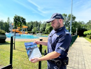 na zdjeciu widać policjanta trzymającego plakat przed basenem