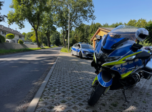Zdjęcie przedstawia motocykl policyjny a w tle radiowóz