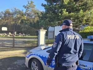 na zdjeciu widać policjanta i radiowóz przed cmentarzem