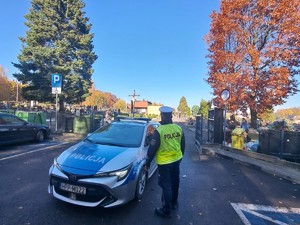 na zdjeciu widać policjanta i radiowóz przed cmentarzem